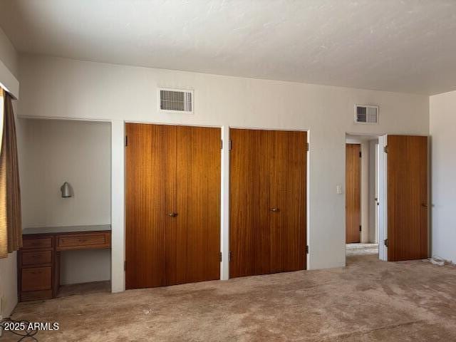 unfurnished bedroom featuring carpet, two closets, and a desk