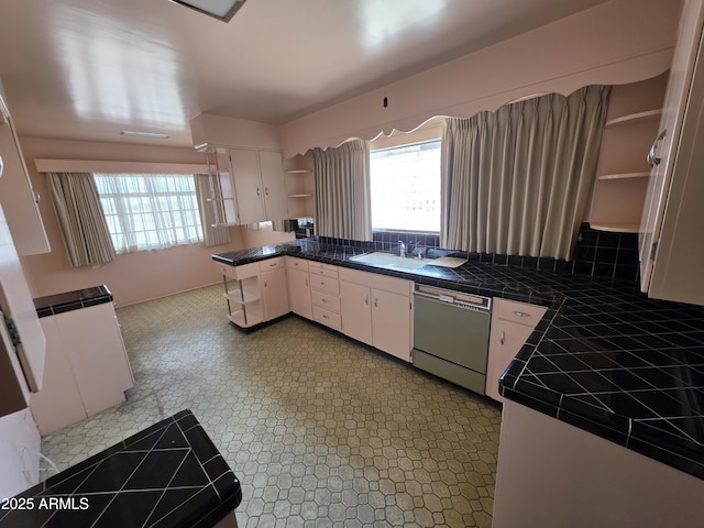 kitchen with open shelves, dishwashing machine, tile countertops, a sink, and healthy amount of natural light