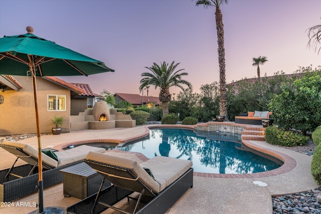 pool at dusk featuring a patio and exterior fireplace