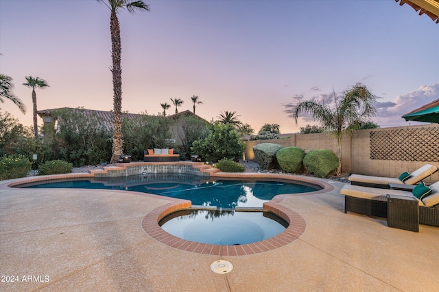 pool at dusk featuring an in ground hot tub and a patio