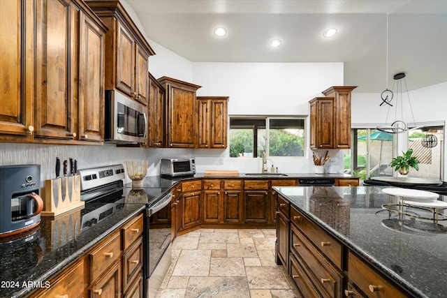 kitchen with dark stone countertops, sink, stainless steel appliances, and hanging light fixtures