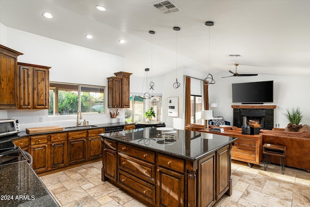 kitchen featuring a tile fireplace, dark stone counters, vaulted ceiling, decorative light fixtures, and a kitchen island