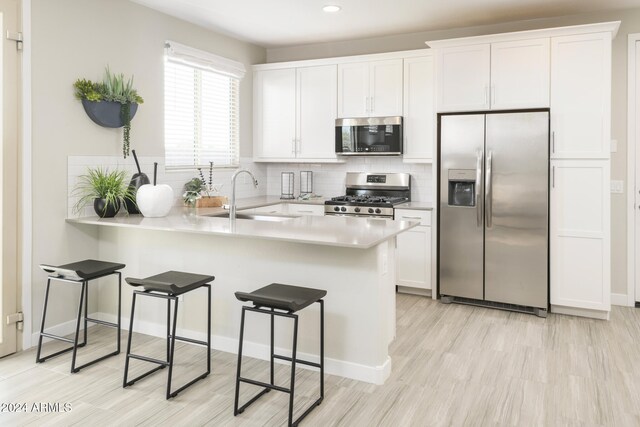 kitchen featuring sink, stainless steel appliances, tasteful backsplash, white cabinets, and kitchen peninsula