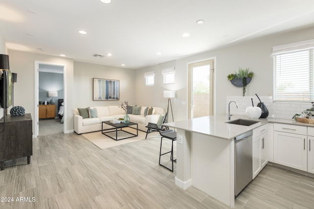 kitchen featuring a breakfast bar, dishwasher, white cabinetry, sink, and kitchen peninsula