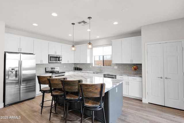 kitchen featuring a kitchen island, appliances with stainless steel finishes, pendant lighting, white cabinetry, and sink