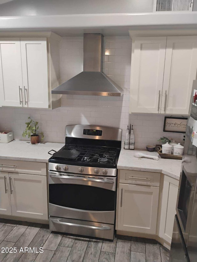 kitchen with light stone counters, tasteful backsplash, gas stove, and wall chimney exhaust hood