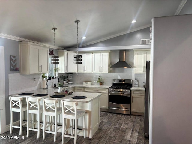 kitchen with pendant lighting, appliances with stainless steel finishes, a kitchen bar, kitchen peninsula, and wall chimney exhaust hood