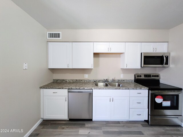 kitchen with appliances with stainless steel finishes, wood-type flooring, white cabinets, and sink