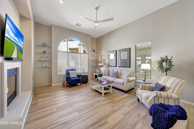 living area with light wood finished floors, baseboards, visible vents, and a glass covered fireplace