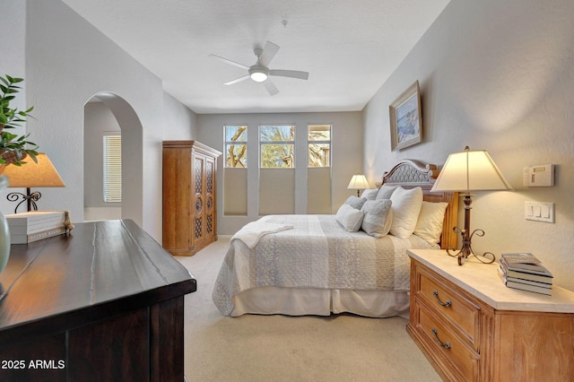 bedroom with arched walkways, ceiling fan, and light colored carpet