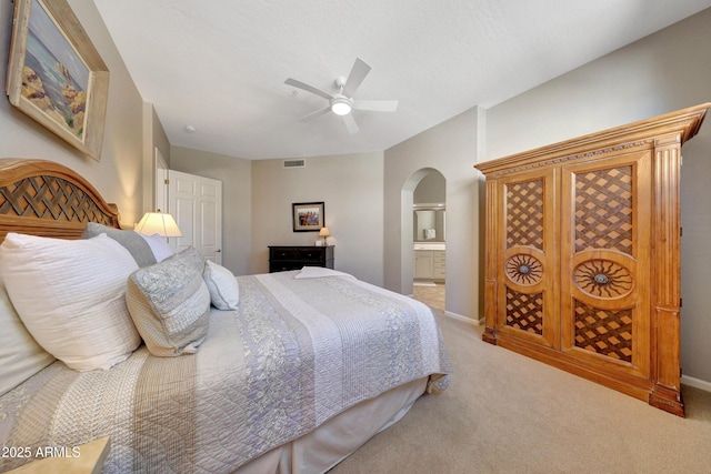 carpeted bedroom featuring arched walkways, connected bathroom, a ceiling fan, visible vents, and baseboards