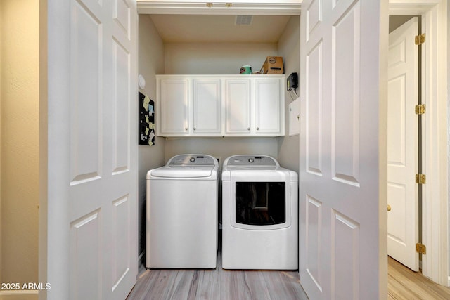 laundry room with washing machine and dryer, visible vents, cabinet space, and light wood-style flooring