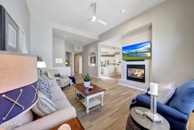 living area with baseboards, ceiling fan, light wood finished floors, and a multi sided fireplace