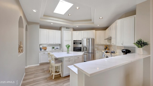 kitchen with appliances with stainless steel finishes, a raised ceiling, visible vents, and under cabinet range hood