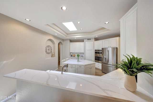 kitchen featuring appliances with stainless steel finishes, a center island, light stone countertops, a tray ceiling, and white cabinetry