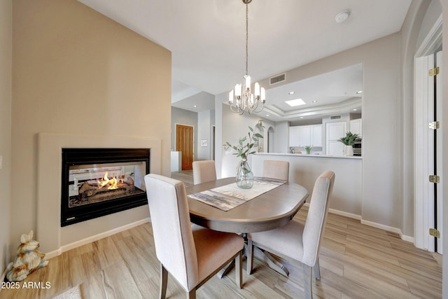 dining room with baseboards, visible vents, a raised ceiling, light wood-type flooring, and a multi sided fireplace