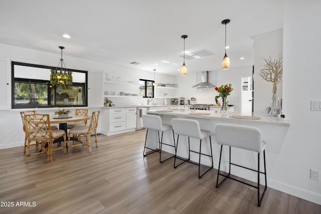 kitchen with wall chimney exhaust hood, a breakfast bar, white cabinetry, light hardwood / wood-style flooring, and dishwasher