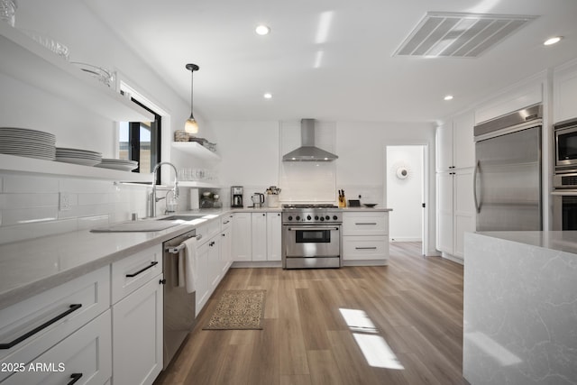 kitchen featuring decorative backsplash, built in appliances, white cabinets, and wall chimney exhaust hood