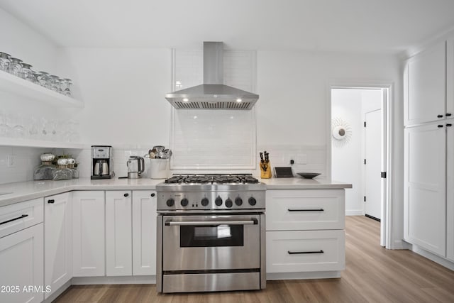 kitchen with tasteful backsplash, high end stainless steel range, light hardwood / wood-style floors, white cabinets, and wall chimney exhaust hood