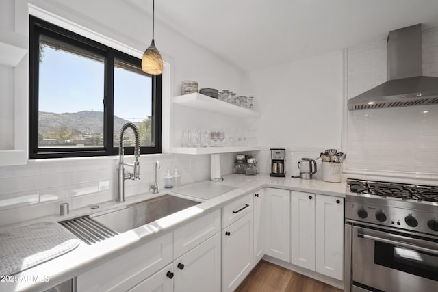 kitchen with white cabinets, high end range, hanging light fixtures, a mountain view, and wall chimney range hood