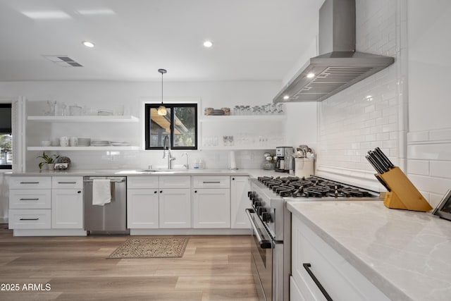 kitchen with white cabinetry, light stone counters, appliances with stainless steel finishes, pendant lighting, and range hood