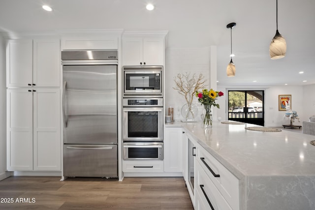 kitchen with pendant lighting, white cabinetry, built in appliances, light stone countertops, and light hardwood / wood-style flooring