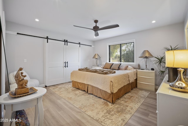 bedroom featuring light hardwood / wood-style floors, a barn door, and ceiling fan