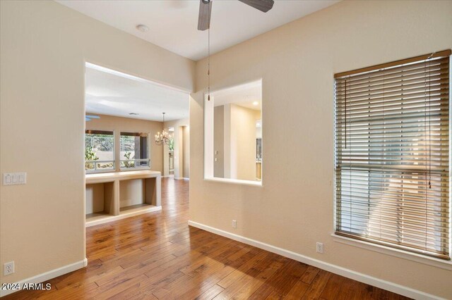 empty room with hardwood / wood-style flooring and ceiling fan with notable chandelier