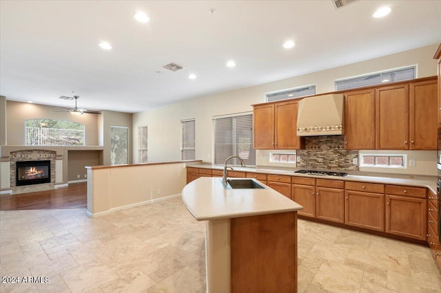 kitchen featuring an island with sink, ventilation hood, ceiling fan, gas cooktop, and sink