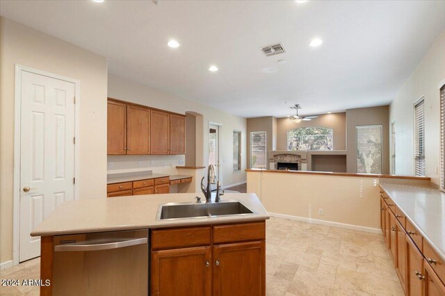 kitchen featuring an island with sink, a fireplace, ceiling fan, stainless steel dishwasher, and sink