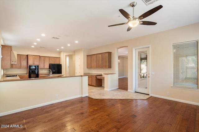 kitchen featuring light hardwood / wood-style floors, kitchen peninsula, black appliances, ceiling fan, and sink