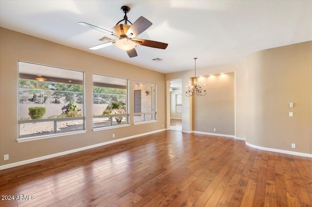 unfurnished room featuring ceiling fan with notable chandelier, hardwood / wood-style floors, and a healthy amount of sunlight