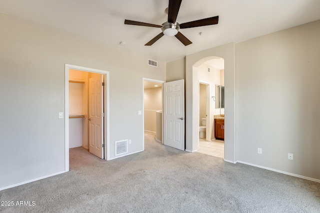 unfurnished bedroom with a walk in closet, ensuite bath, ceiling fan, light colored carpet, and a closet