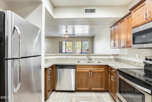 kitchen with backsplash, sink, ceiling fan, light stone counters, and stainless steel appliances