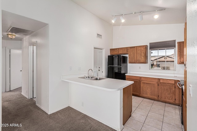 kitchen with light tile patterned flooring, vaulted ceiling, black refrigerator, sink, and kitchen peninsula