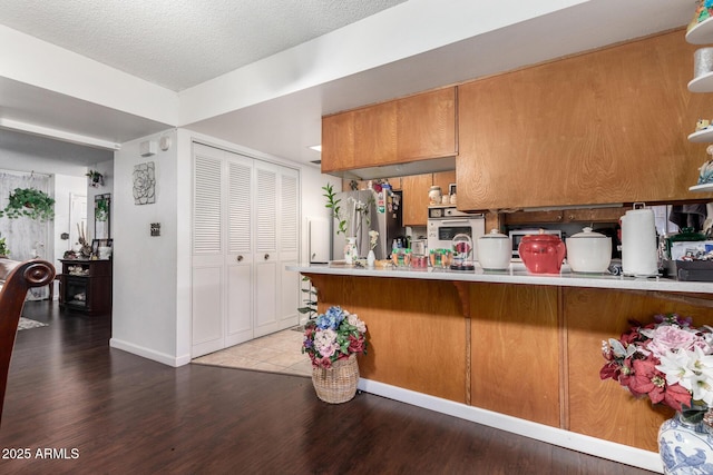 kitchen featuring kitchen peninsula, a textured ceiling, hardwood / wood-style flooring, stainless steel fridge, and white oven