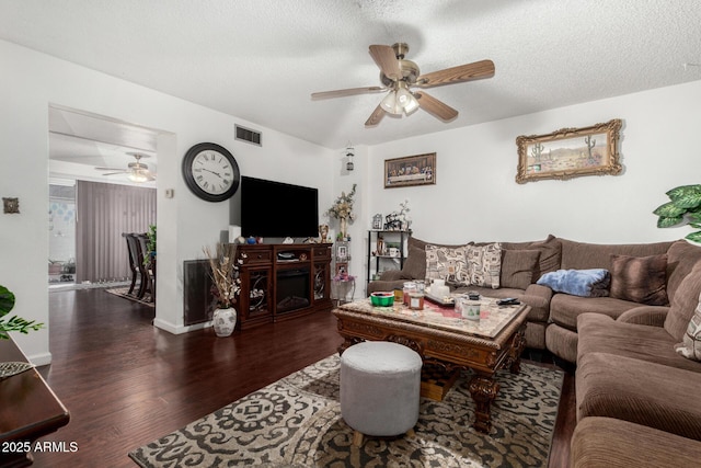 living room with a textured ceiling, dark wood-type flooring, and ceiling fan