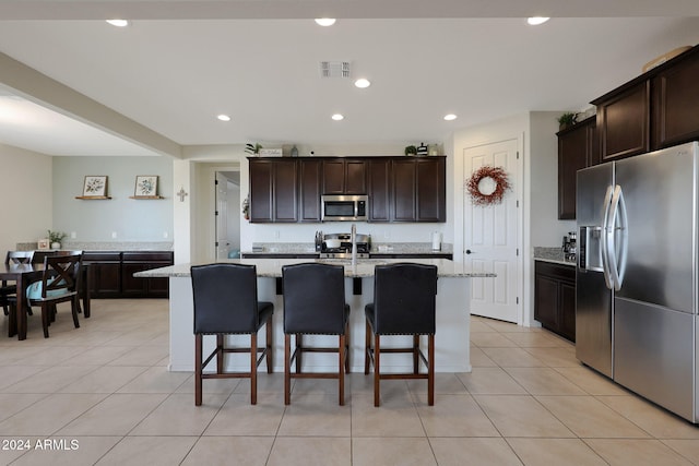 kitchen featuring light stone countertops, appliances with stainless steel finishes, a kitchen island with sink, and light tile patterned flooring