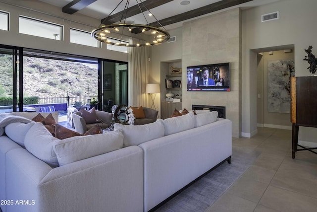 tiled living room with a notable chandelier, beam ceiling, a fireplace, and a towering ceiling