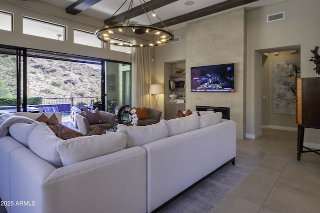 tiled living room with a chandelier, a towering ceiling, beam ceiling, and a tiled fireplace