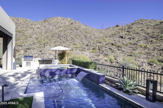 exterior space with an in ground hot tub, area for grilling, a mountain view, pool water feature, and an outdoor kitchen