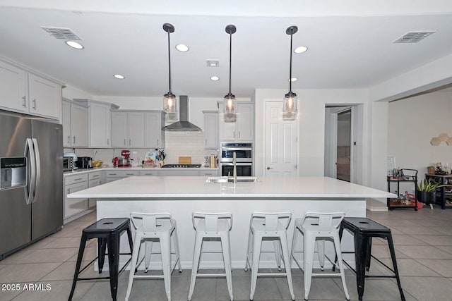 kitchen featuring a kitchen island with sink, a kitchen breakfast bar, wall chimney exhaust hood, and appliances with stainless steel finishes