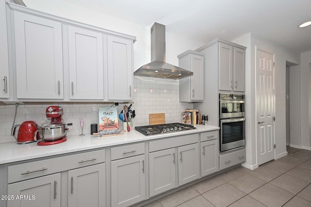 kitchen featuring stainless steel appliances, light tile patterned flooring, backsplash, and wall chimney exhaust hood