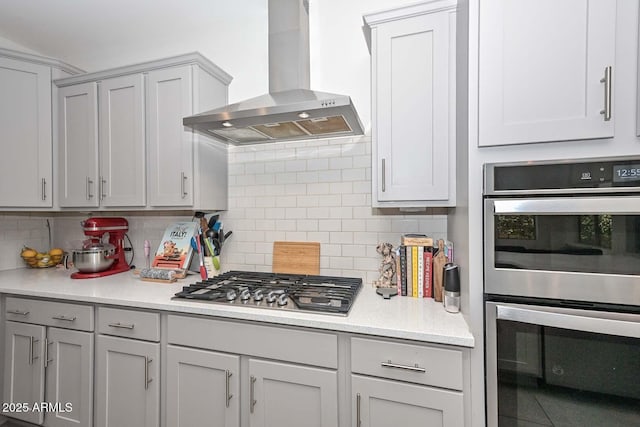 kitchen with backsplash, gray cabinets, stainless steel appliances, and wall chimney exhaust hood