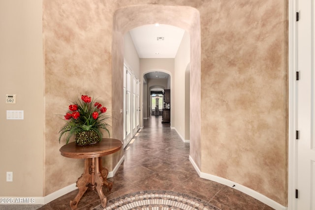 hall featuring arched walkways and baseboards
