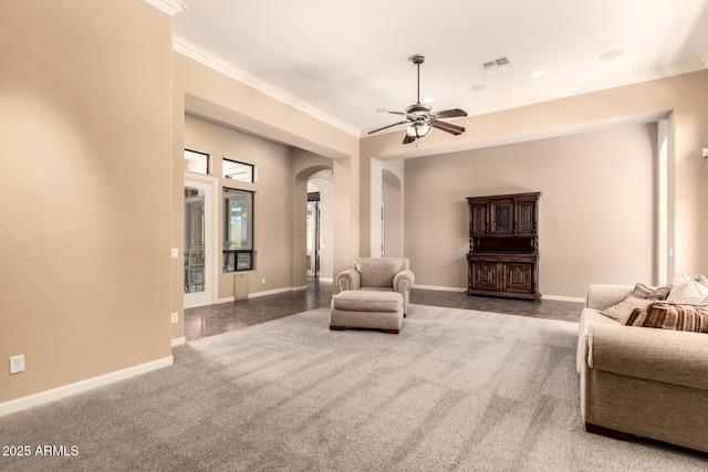 carpeted living room with arched walkways, ornamental molding, a ceiling fan, and baseboards