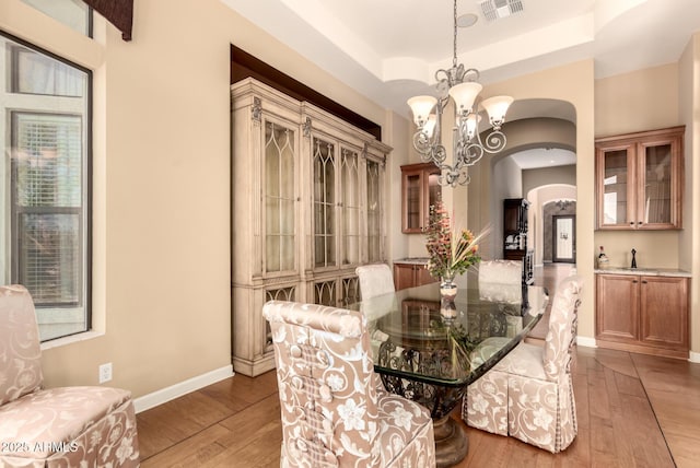 dining area with arched walkways, hardwood / wood-style flooring, a chandelier, baseboards, and a raised ceiling