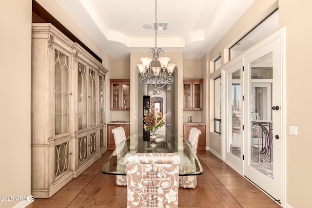 dining room with a chandelier, a raised ceiling, hardwood / wood-style flooring, and baseboards