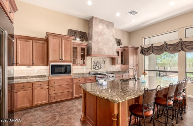 kitchen featuring a sink, high end appliances, backsplash, stone counters, and brown cabinetry