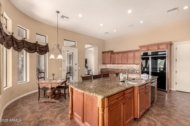 kitchen featuring a sink, stainless steel dishwasher, refrigerator, an island with sink, and arched walkways